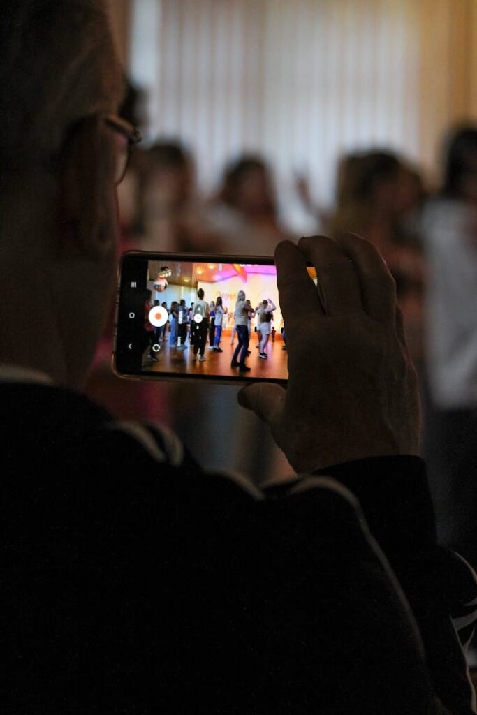 photo-17722043 Senior adult recording a vibrant dance show using smartphone indoors.